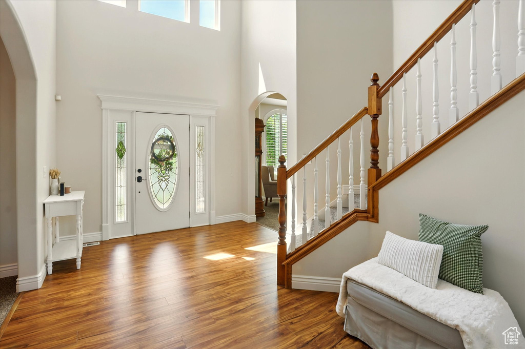 Entryway with arched walkways, healthy amount of natural light, wood finished floors, a high ceiling, and baseboards