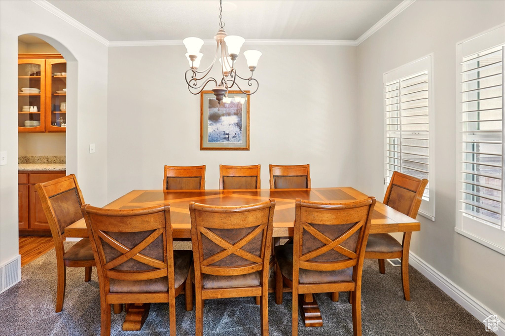 Carpeted dining room with a chandelier, ornamental molding, baseboards, and arched walkways