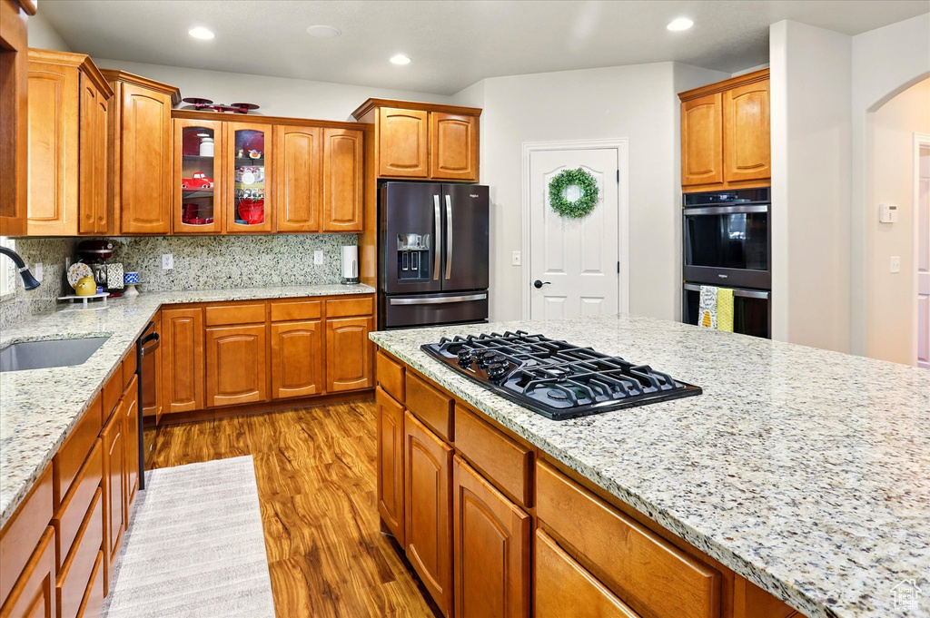 Kitchen with refrigerator with ice dispenser, black gas cooktop, a sink, light wood-style floors, and arched walkways