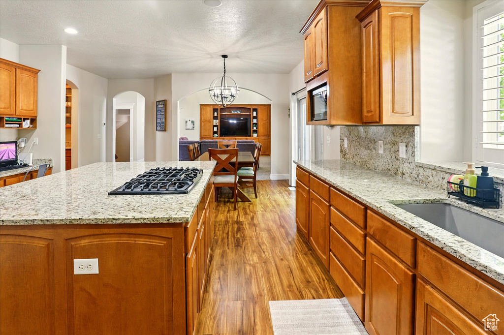 Kitchen featuring black gas stovetop, arched walkways, wood finished floors, a center island, and light stone countertops