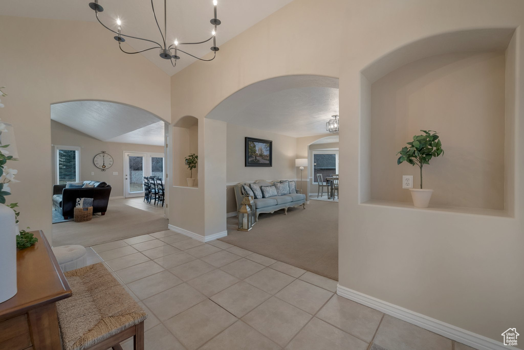 Entrance foyer with arched walkways, light colored carpet, light tile patterned floors, a chandelier, and high vaulted ceiling