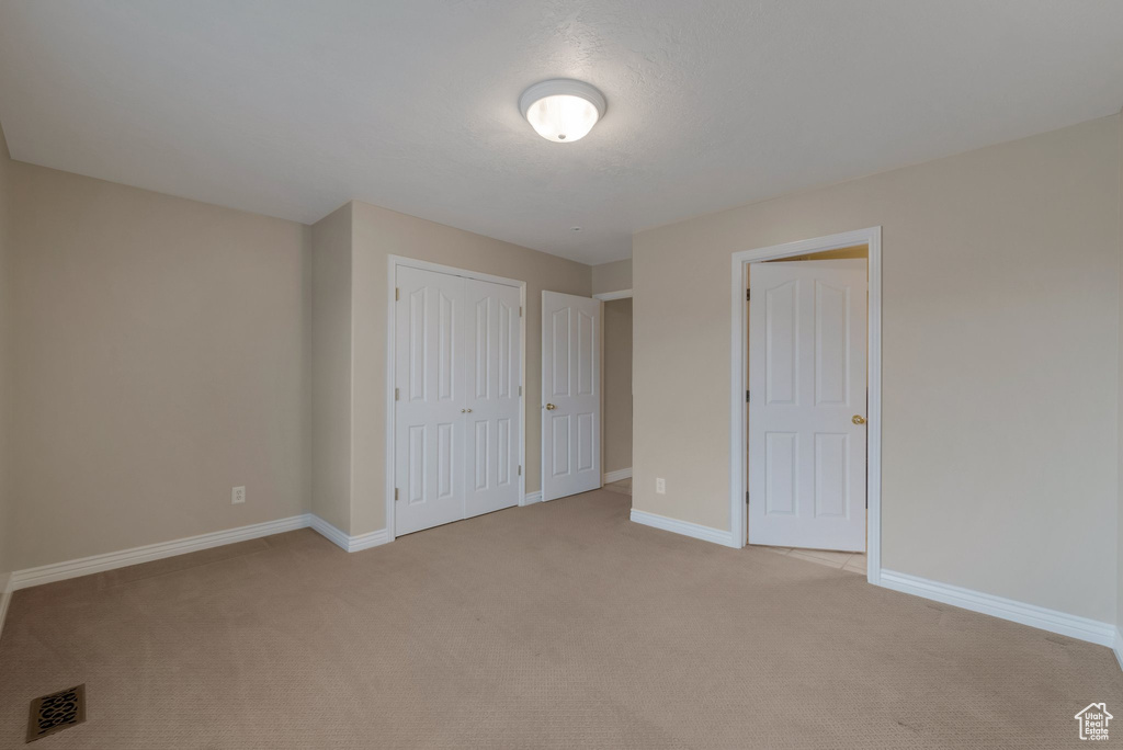 Unfurnished bedroom featuring light colored carpet, baseboards, and a closet