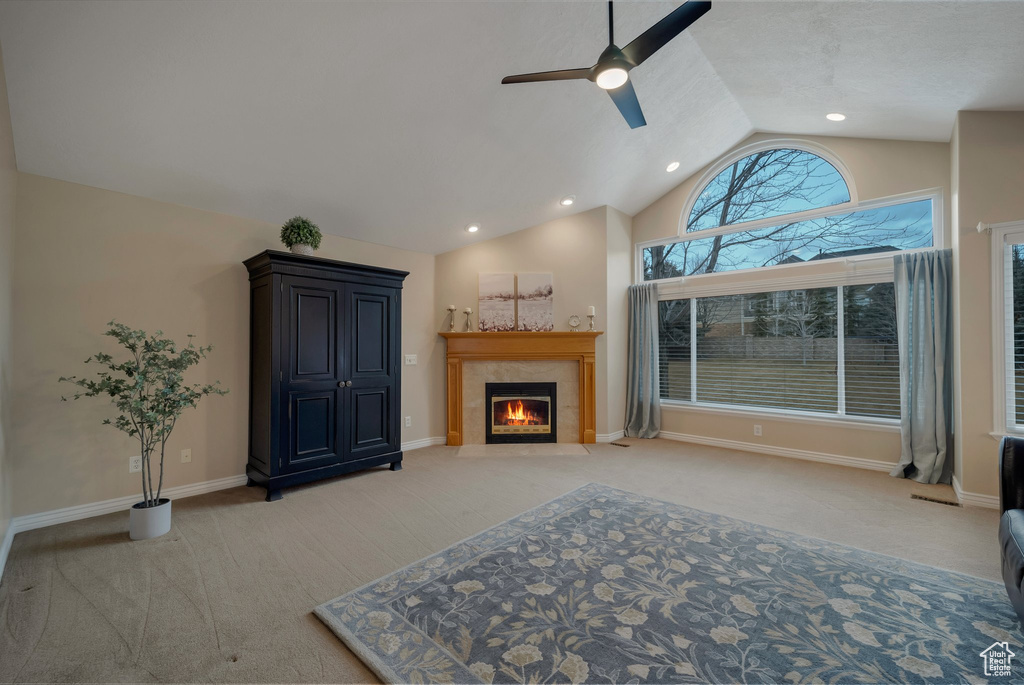 Living area with a tiled fireplace, light colored carpet, vaulted ceiling, ceiling fan, and baseboards