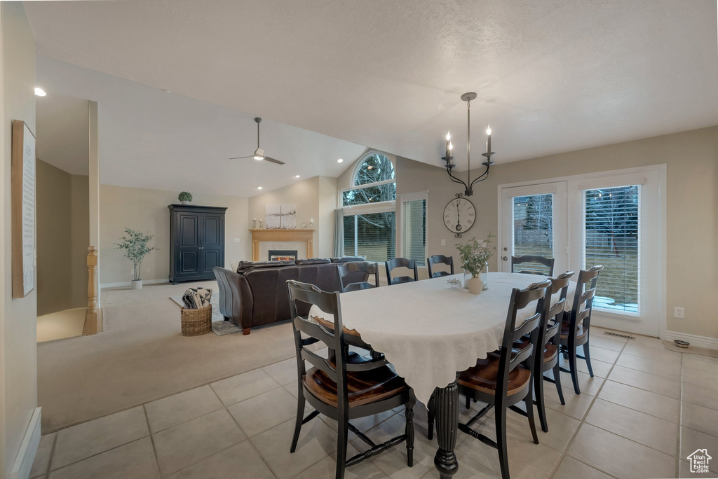 Dining area with light tile patterned flooring, baseboards, a warm lit fireplace, lofted ceiling, and ceiling fan