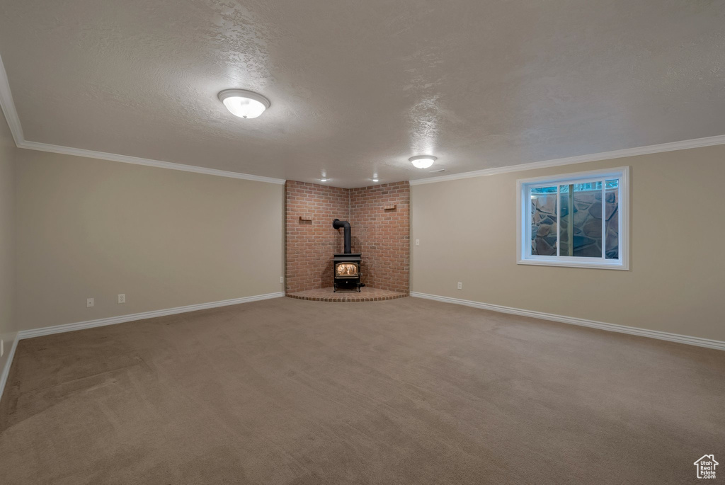 Unfurnished living room with a wood stove, a textured ceiling, baseboards, ornamental molding, and carpet floors