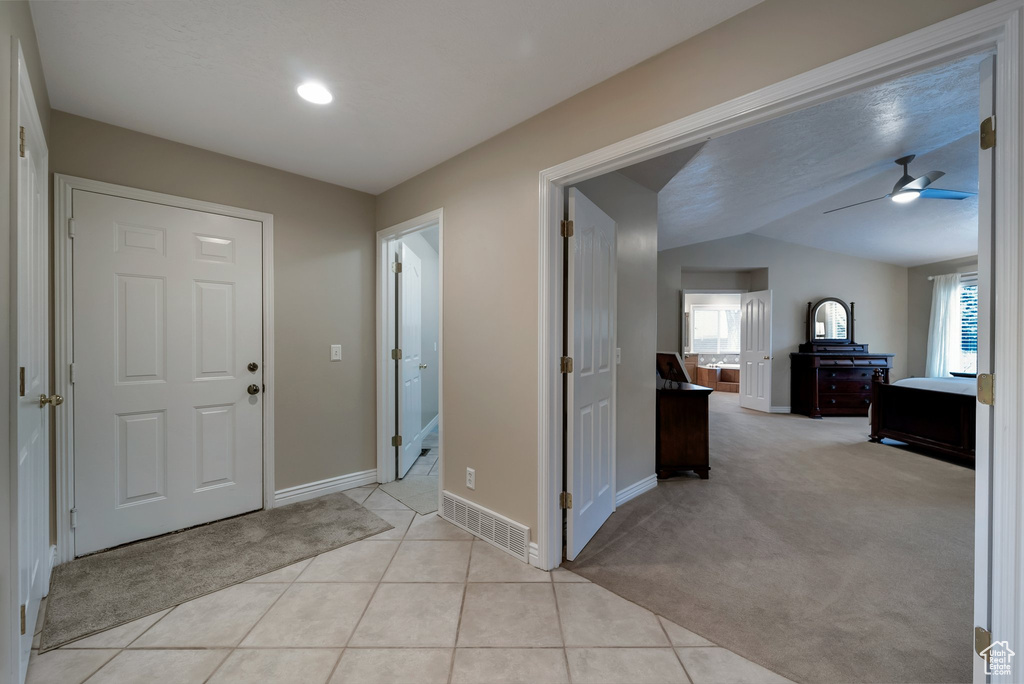 Foyer with baseboards, ceiling fan, light tile patterned floors, light colored carpet, and vaulted ceiling
