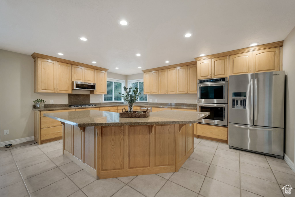 Kitchen with appliances with stainless steel finishes, light brown cabinets, a center island, recessed lighting, and light tile patterned floors
