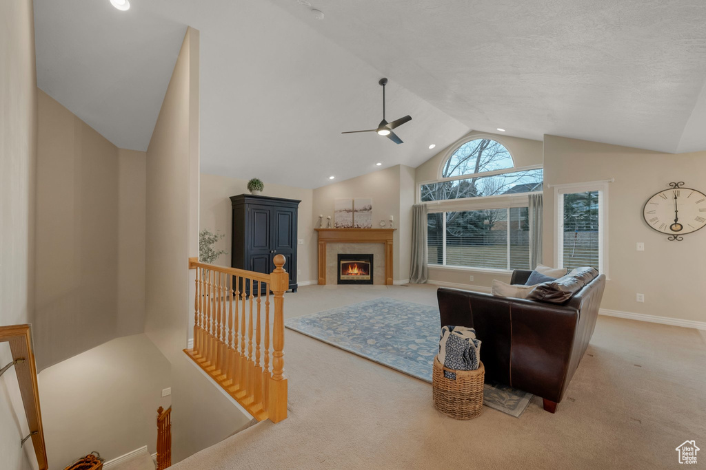 Living room with carpet flooring, ceiling fan, a fireplace, baseboards, and high vaulted ceiling