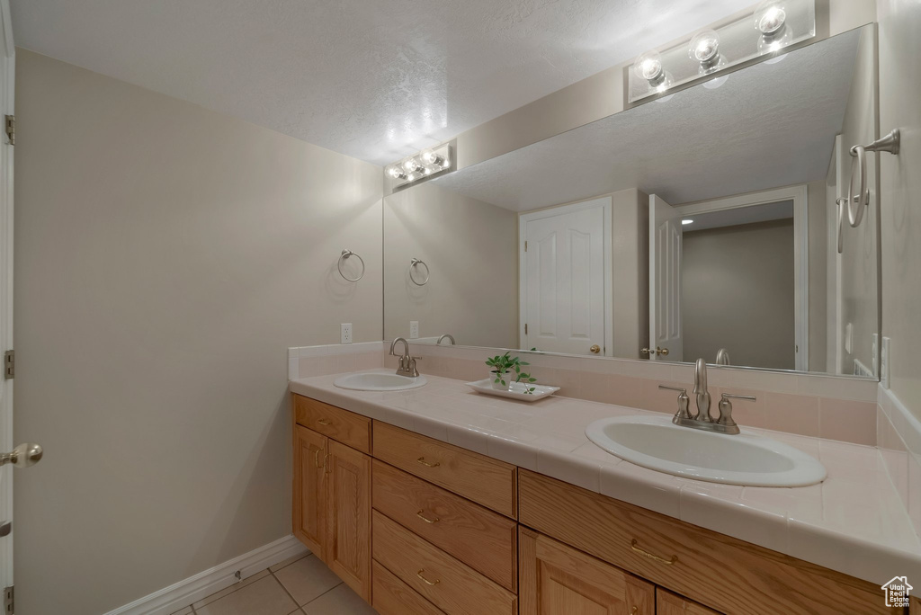 Full bathroom featuring double vanity, tile patterned flooring, baseboards, and a textured ceiling