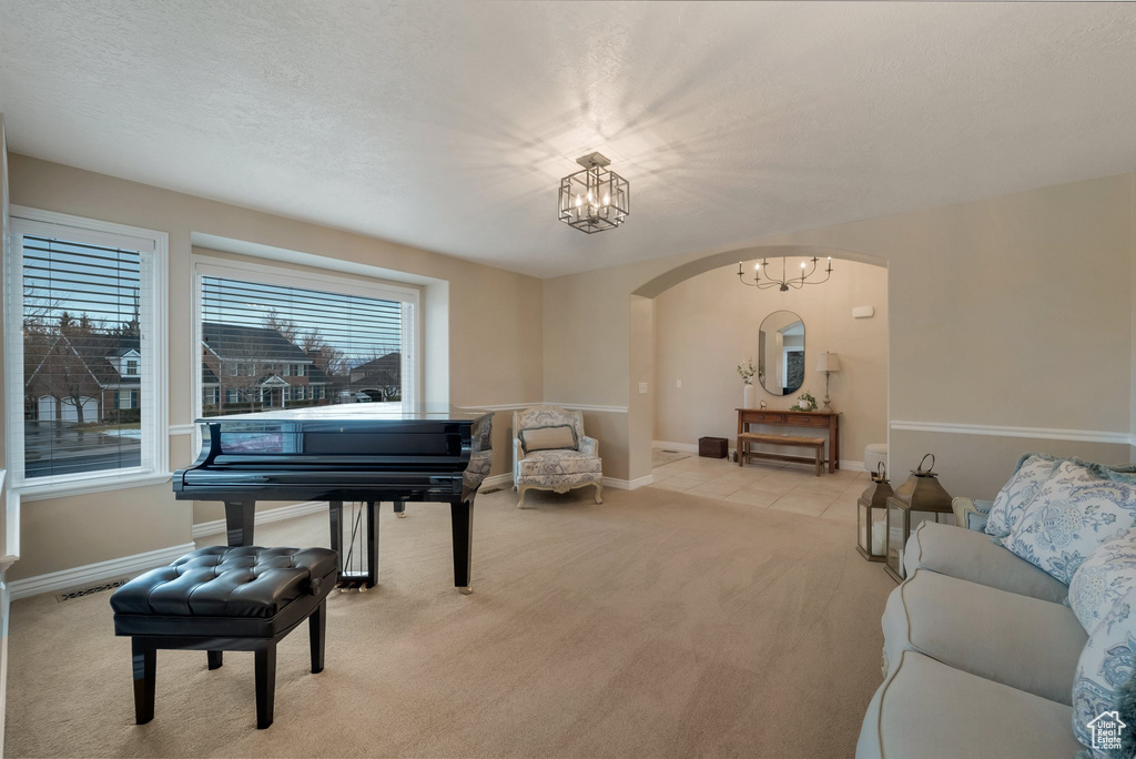 Sitting room with arched walkways, light colored carpet, a chandelier, and baseboards