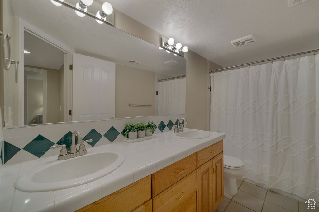 Full bathroom featuring double vanity, toilet, tile patterned flooring, decorative backsplash, and a shower with curtain