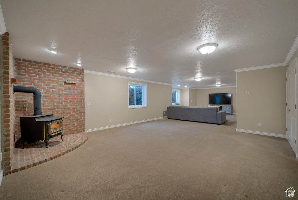 Unfurnished living room with a wood stove, carpet flooring, ornamental molding, baseboards, and a textured ceiling