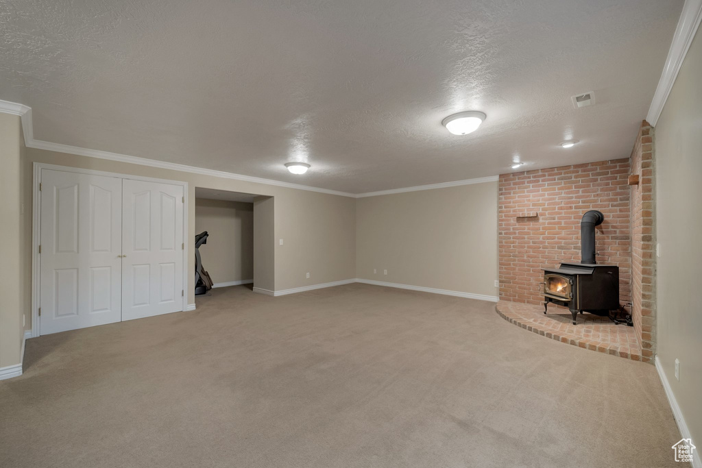 Finished basement featuring a textured ceiling, a wood stove, baseboards, light colored carpet, and ornamental molding
