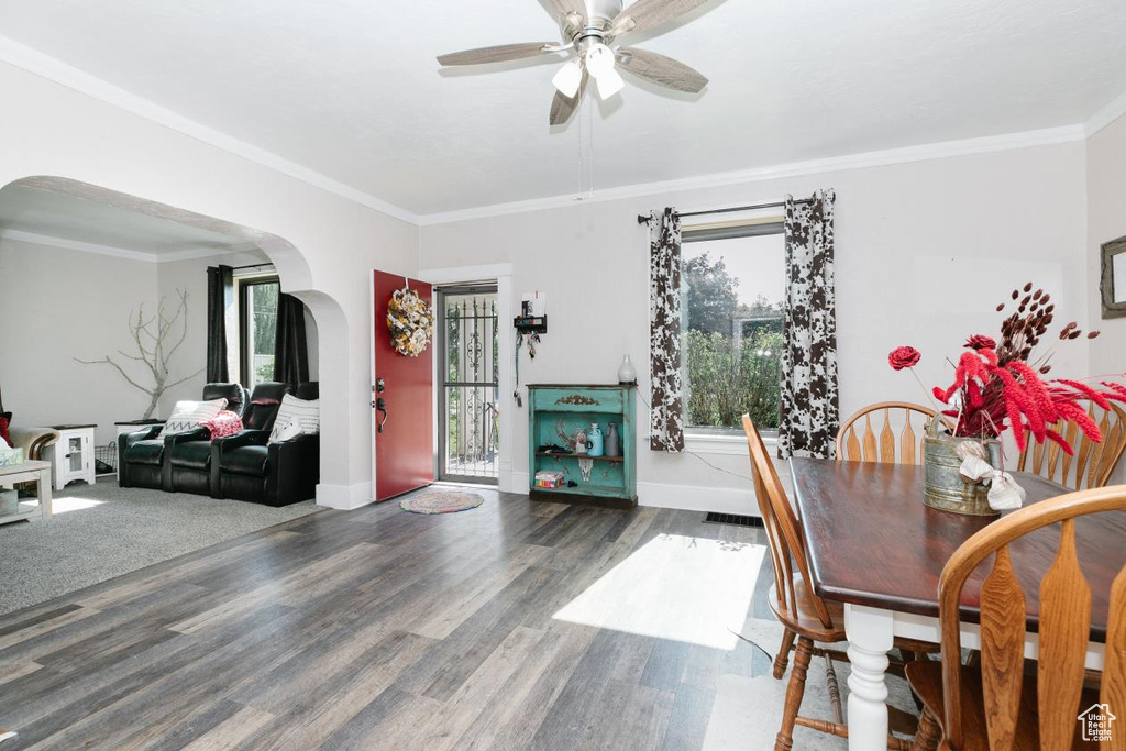 Dining room featuring arched walkways, a ceiling fan, ornamental molding, baseboards, and wood finished floors