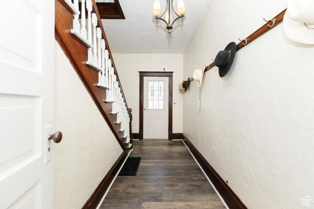 Doorway to outside with a textured wall, baseboards, a chandelier, dark wood-style flooring, and stairway
