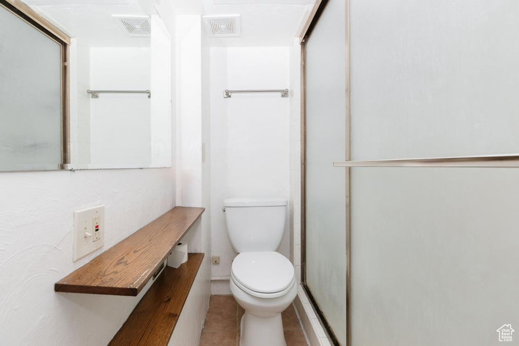 Full bathroom with toilet, tile patterned floors, and a shower with door