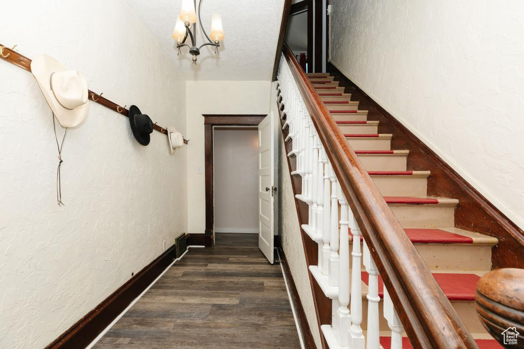 Stairs featuring wood finished floors, a chandelier, and a textured wall