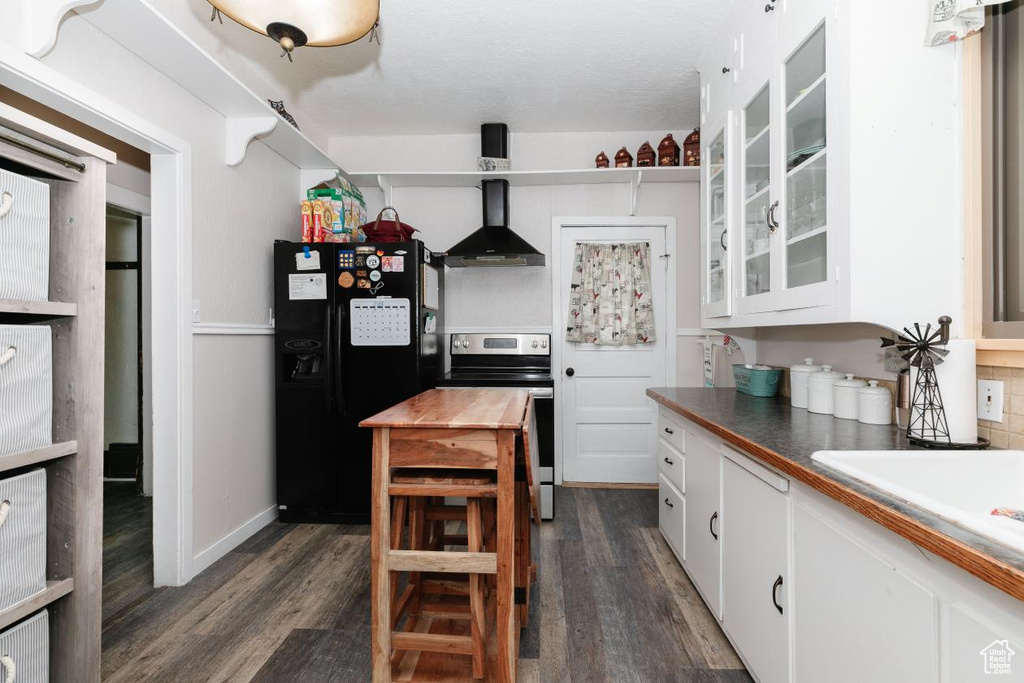 Kitchen featuring wall chimney range hood, black refrigerator with ice dispenser, stainless steel electric range, and dark wood-type flooring
