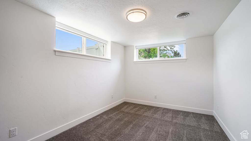 Empty room featuring dark carpet, baseboards, and a textured ceiling