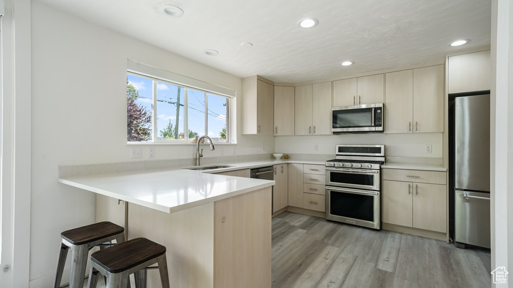 Kitchen with stainless steel appliances, a sink, a peninsula, a kitchen bar, and light countertops