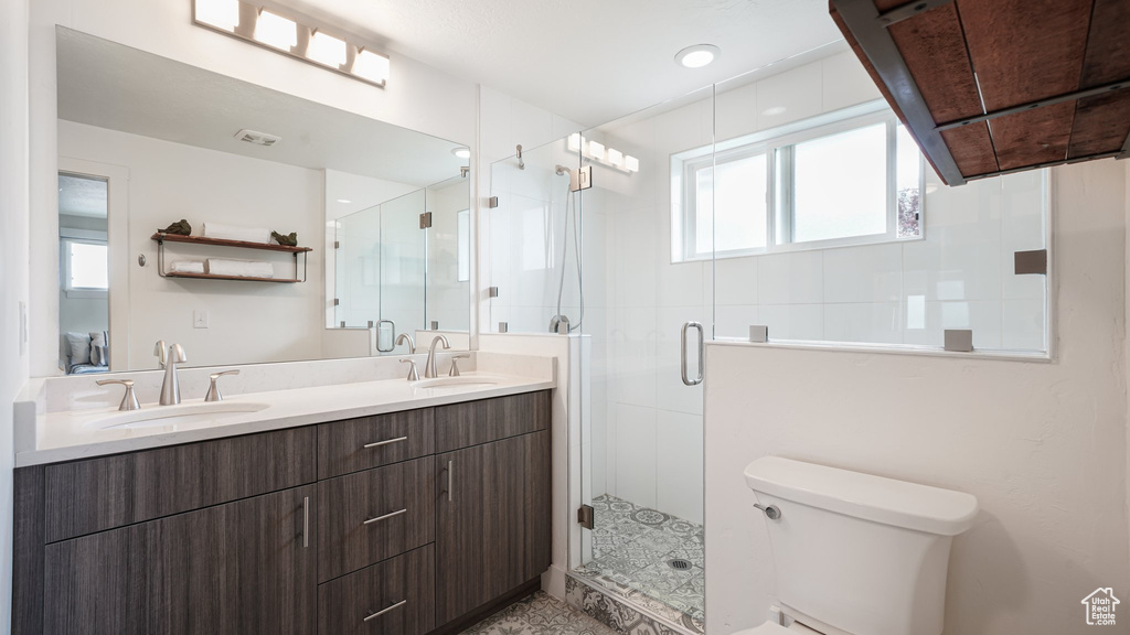 Full bath featuring healthy amount of natural light, toilet, double vanity, and a stall shower