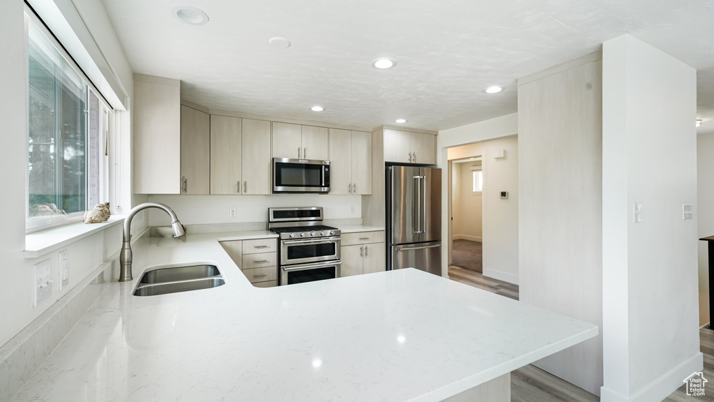 Kitchen featuring appliances with stainless steel finishes, a sink, recessed lighting, a peninsula, and light stone counters