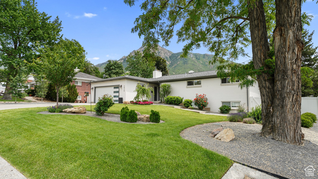 Ranch-style house featuring a chimney, a mountain view, a garage, and a front lawn