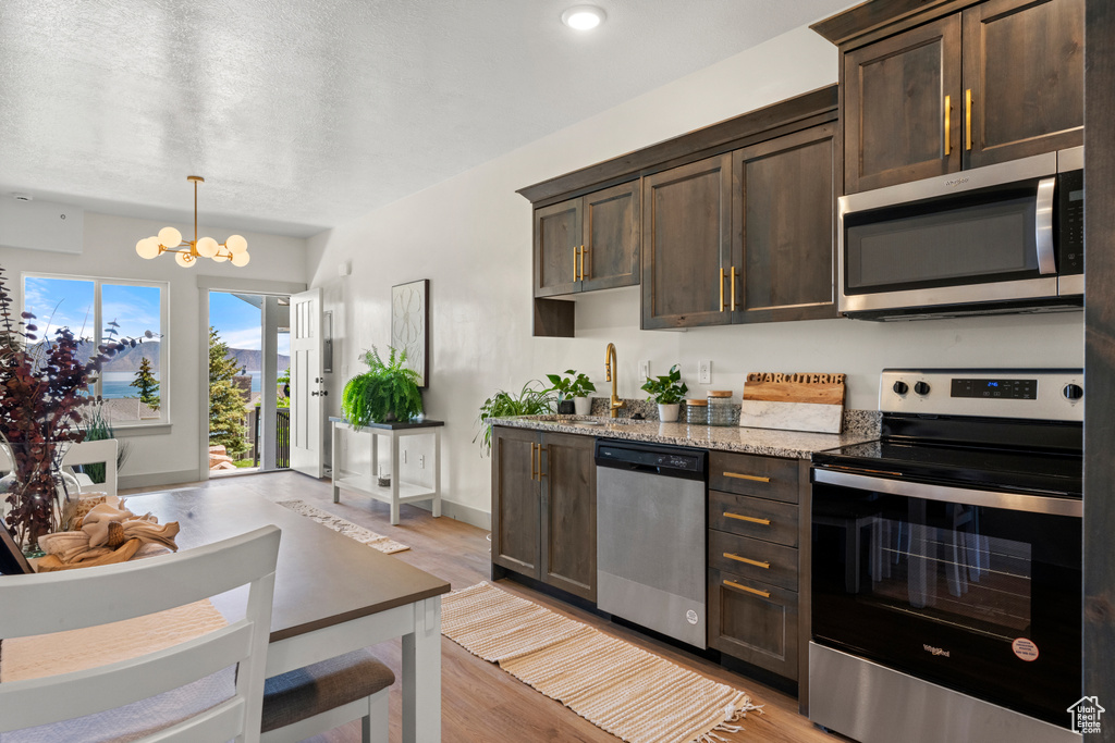 Kitchen with appliances with stainless steel finishes, dark brown cabinets, a chandelier, and recessed lighting