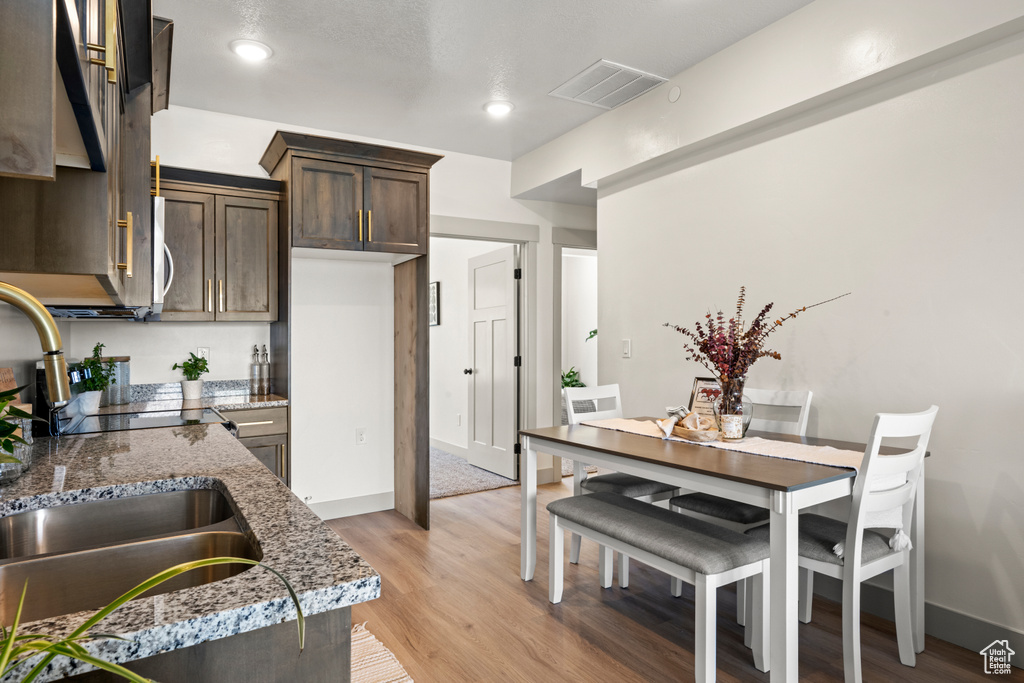 Kitchen featuring dark brown cabinets, light wood finished floors, light stone counters, and recessed lighting