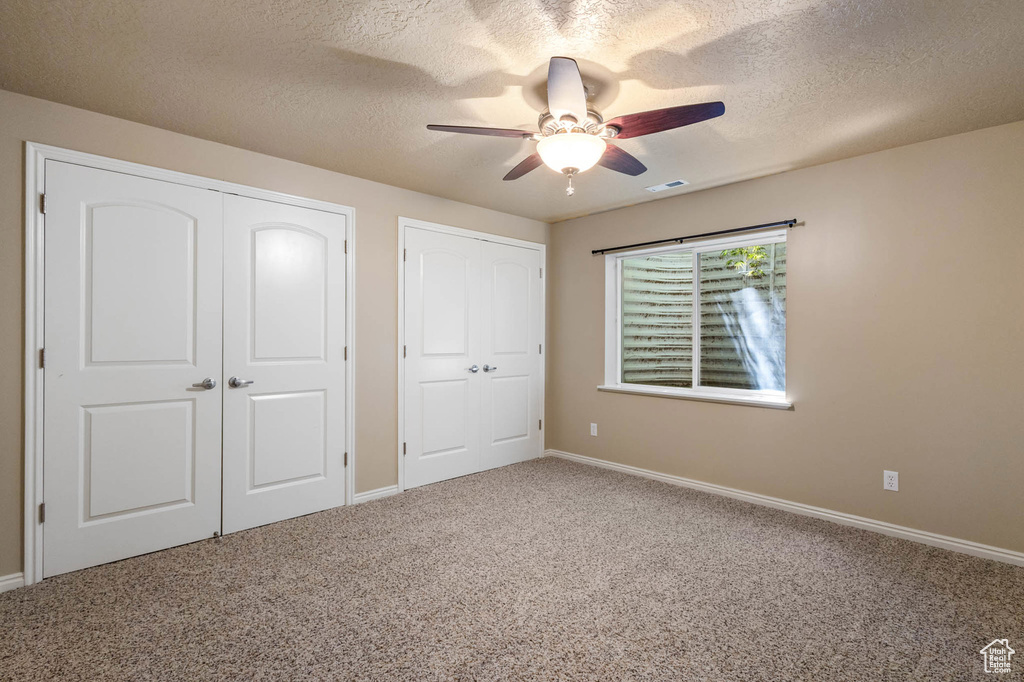 Unfurnished bedroom featuring carpet flooring, a textured ceiling, baseboards, and a ceiling fan