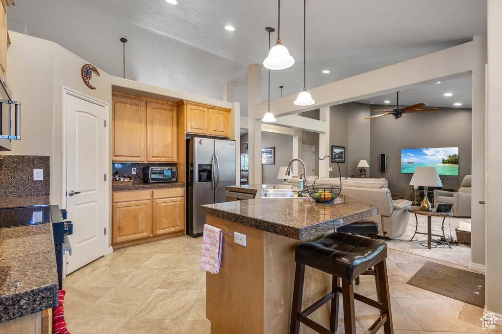 Kitchen featuring appliances with stainless steel finishes, a sink, tile counters, a breakfast bar area, and open floor plan