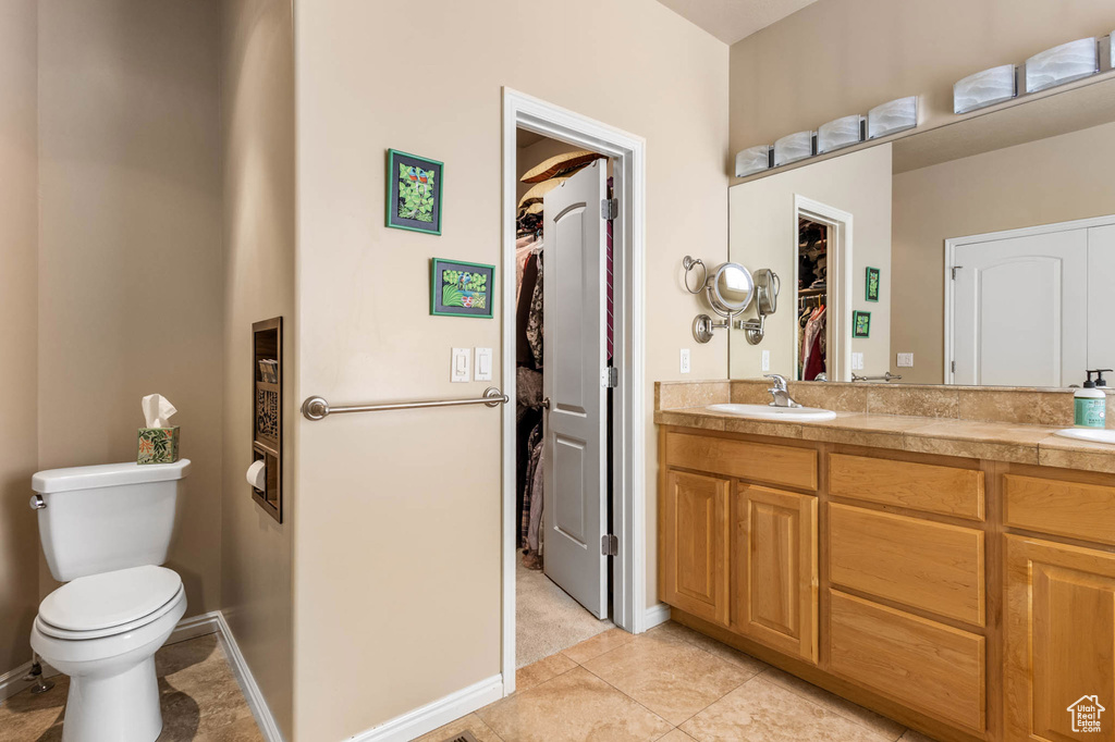 Bathroom featuring a spacious closet, double vanity, toilet, tile patterned floors, and baseboards