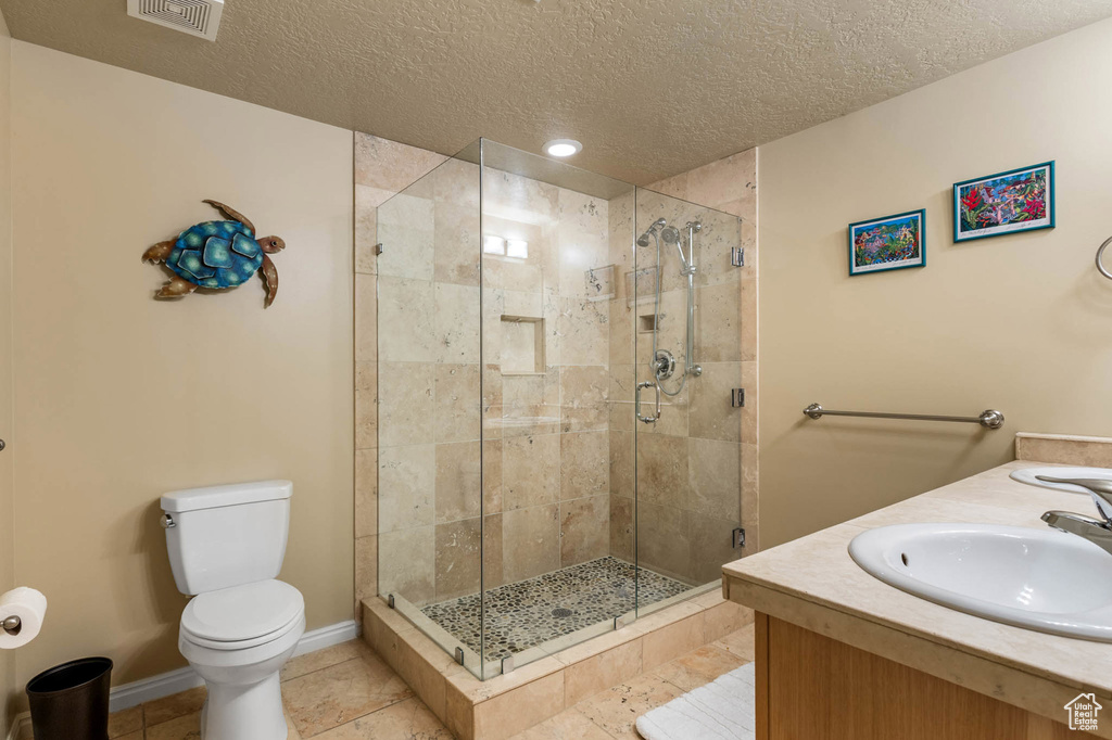 Full bath featuring toilet, a shower stall, a textured ceiling, vanity, and baseboards