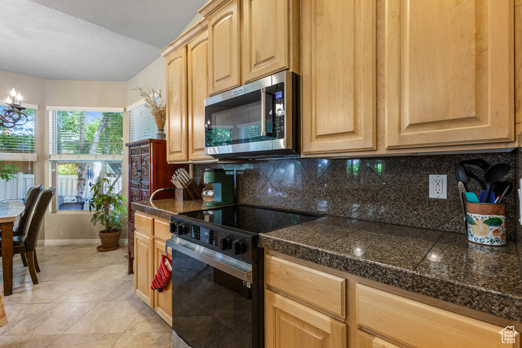 Kitchen featuring stainless steel microwave, tile counters, black electric range, tasteful backsplash, and baseboards