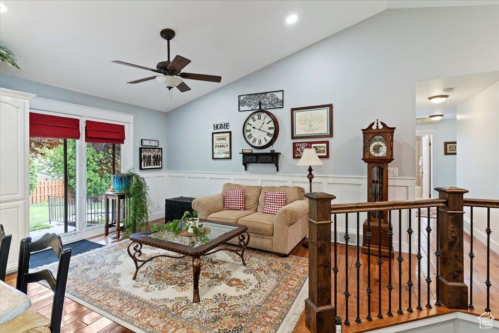 Living area with vaulted ceiling, wood finished floors, a ceiling fan, wainscoting, and a decorative wall