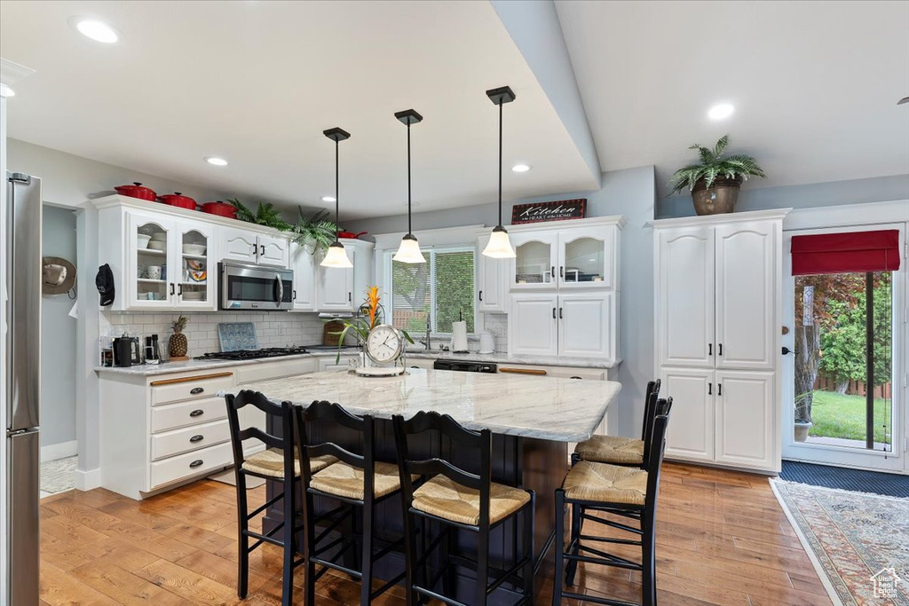 Kitchen with stainless steel appliances, a breakfast bar, white cabinetry, glass insert cabinets, and recessed lighting