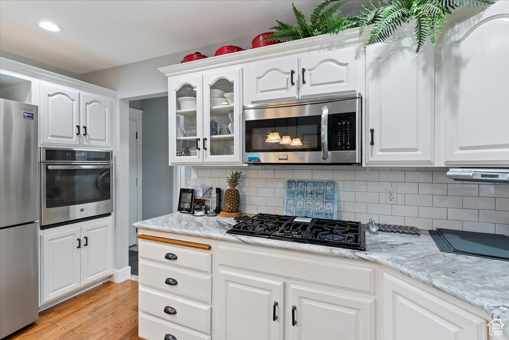 Kitchen with appliances with stainless steel finishes, light wood finished floors, white cabinets, glass insert cabinets, and recessed lighting