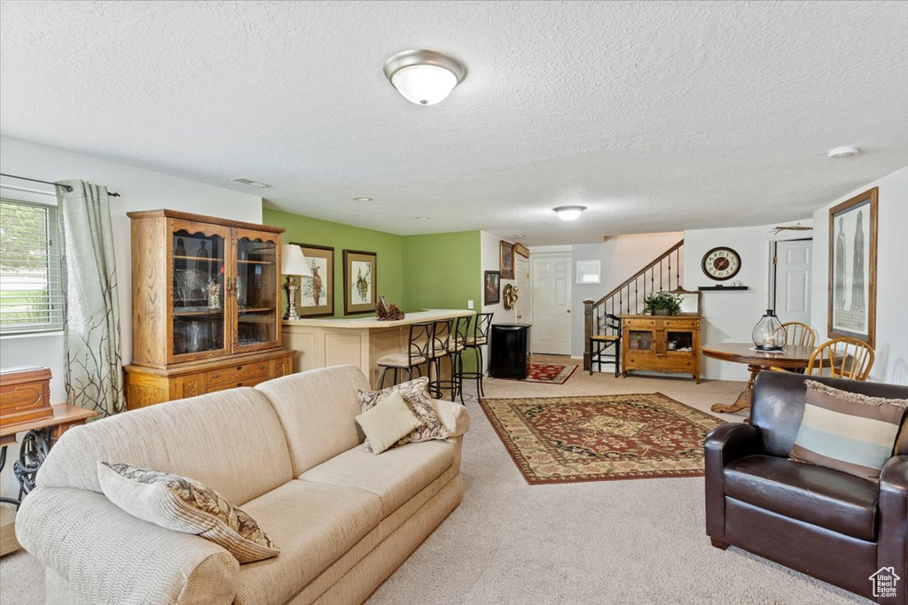 Living area with stairs, a textured ceiling, and light colored carpet