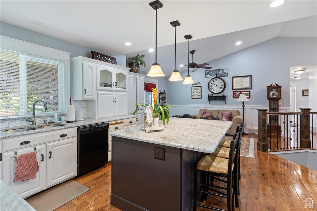 Kitchen featuring dishwasher, a sink, a kitchen island, a ceiling fan, and a breakfast bar