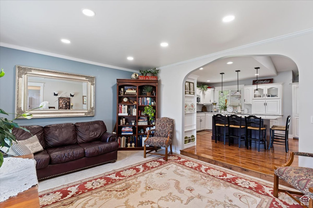 Living room with arched walkways, recessed lighting, crown molding, and light wood-type flooring