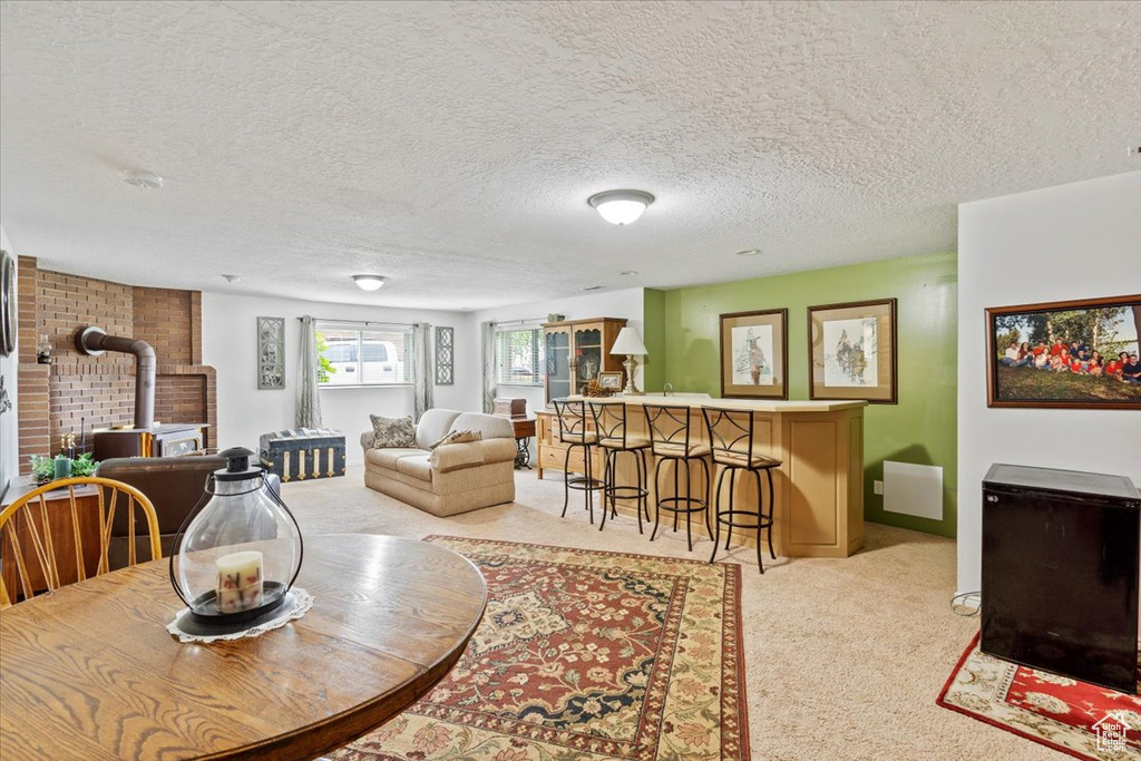 Dining space with a wood stove, light carpet, a textured ceiling, and baseboards