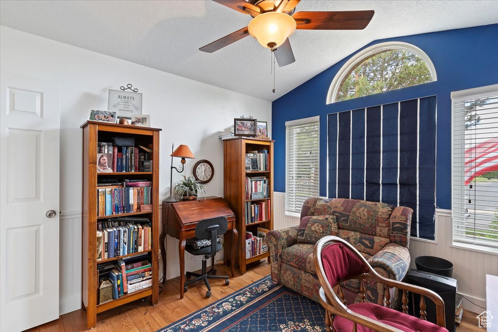 Sitting room featuring vaulted ceiling, ceiling fan, wood finished floors, wainscoting, and a textured ceiling