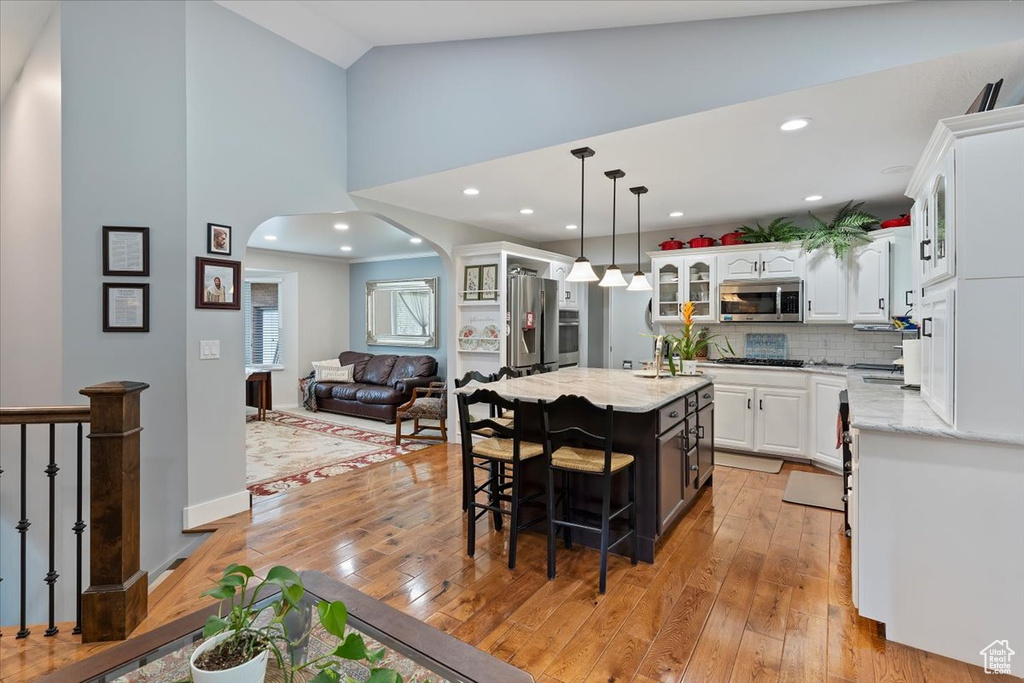Kitchen with stainless steel appliances, arched walkways, light wood-type flooring, white cabinets, and glass insert cabinets
