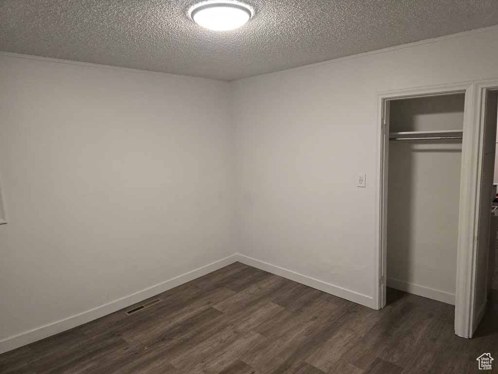 Unfurnished bedroom with dark wood-style flooring, a closet, a textured ceiling, and baseboards