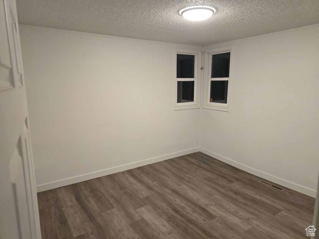 Unfurnished room featuring a textured ceiling, dark wood-style flooring, and baseboards