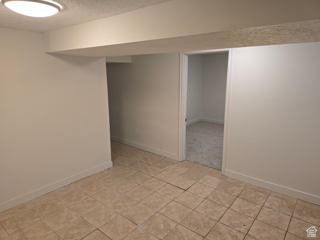 Finished basement featuring a textured ceiling, light tile patterned floors, and baseboards