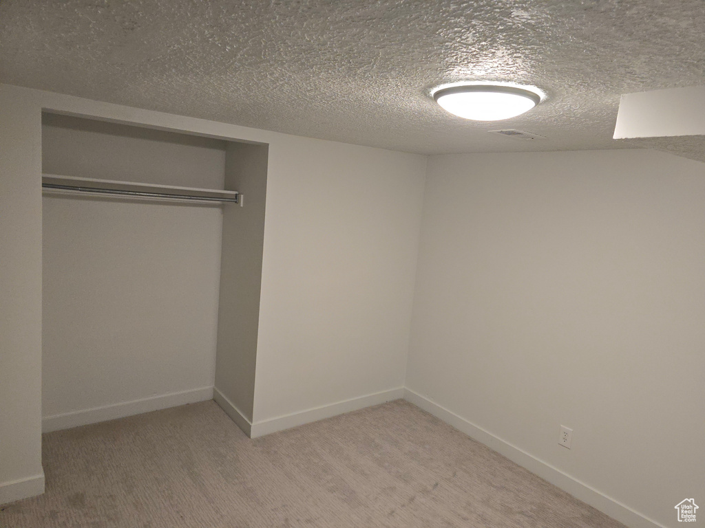 Unfurnished bedroom featuring a closet, baseboards, light colored carpet, and a textured ceiling