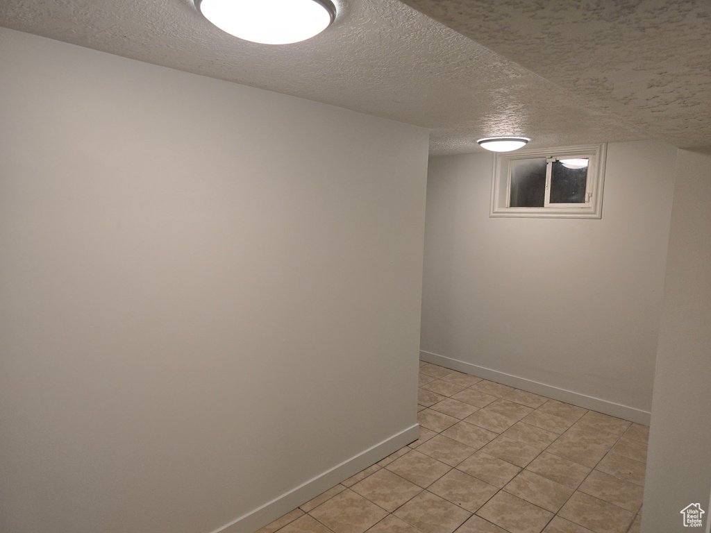 Finished below grade area with a textured ceiling, baseboards, and light tile patterned floors