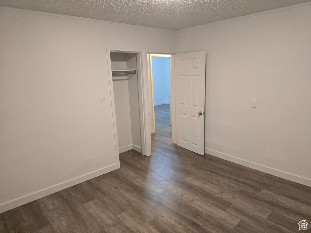 Unfurnished bedroom featuring dark wood-type flooring, a textured ceiling, and baseboards