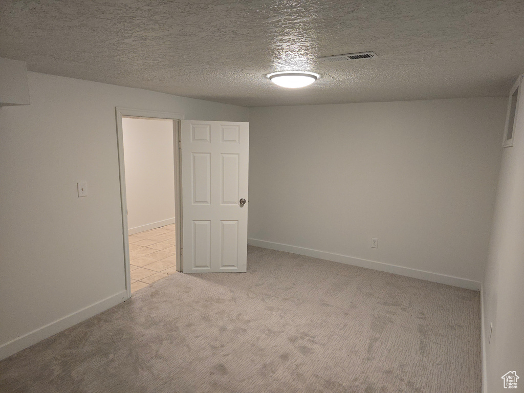 Unfurnished room featuring light colored carpet, baseboards, and a textured ceiling
